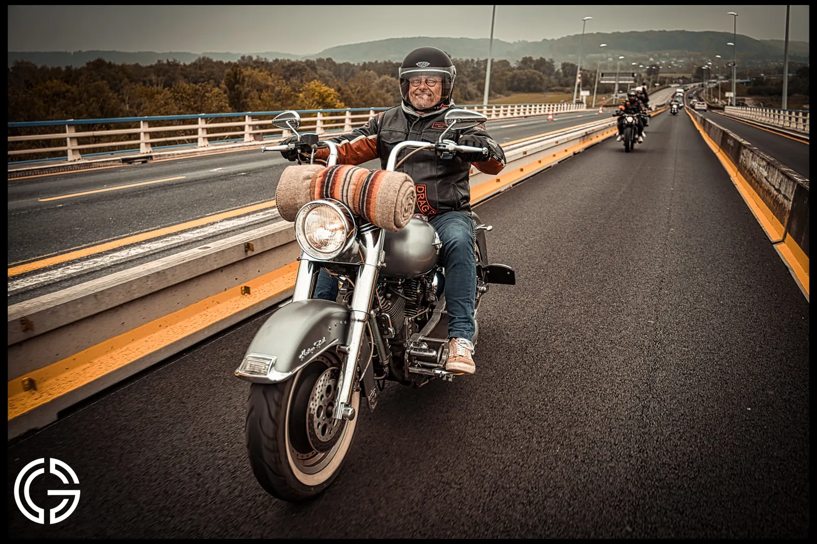Un motard sur une Harley-Davidson traverse un pont, suivi d'autres motos.