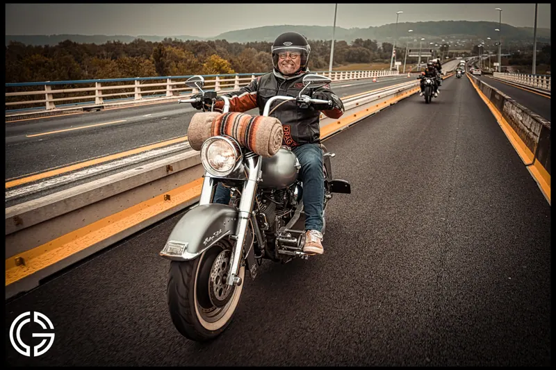 Un motard sur une Harley-Davidson traverse un pont, suivi d'autres motos.