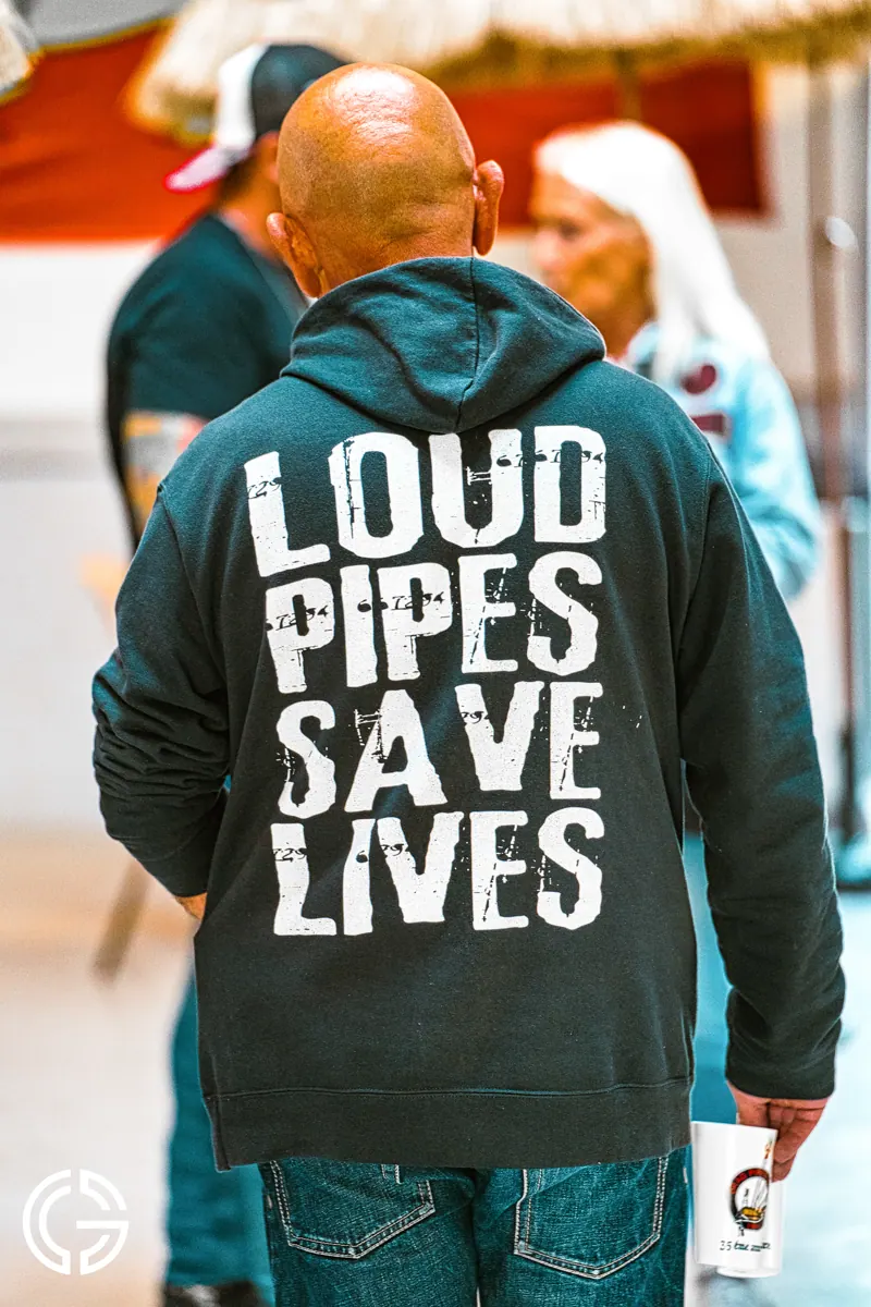 De dos dans la foule, un homme porte un sweat « Loud pipes save lives ».