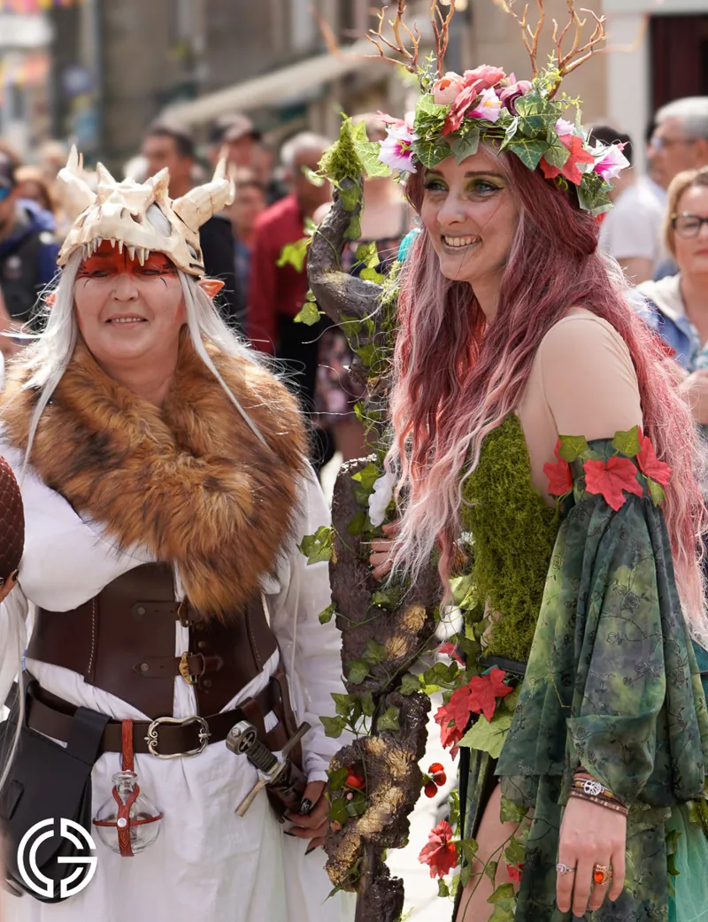 Deux femmes costumées dans la foule, l'une coiffée d'un casque à cornes, l'autre d'une couronne de fleurs.
