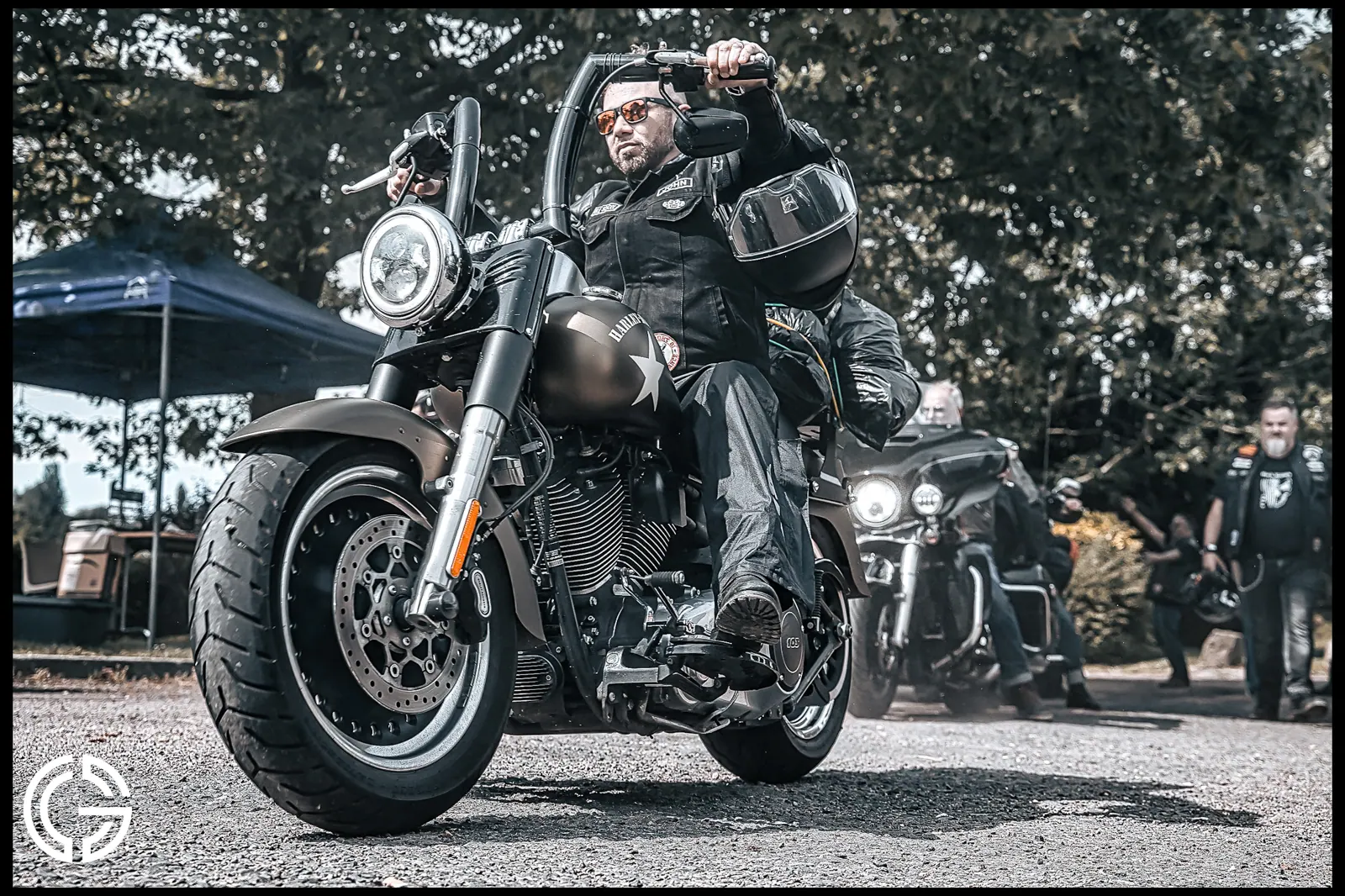 Un biker en blouson de cuir arrêté sur sa Harley-Davidson, d'autres motos derrière lui.