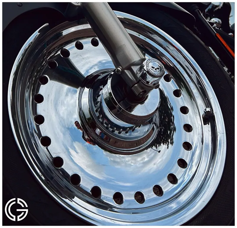 Gros plan sur une roue chromée de moto qui reflète le ciel.