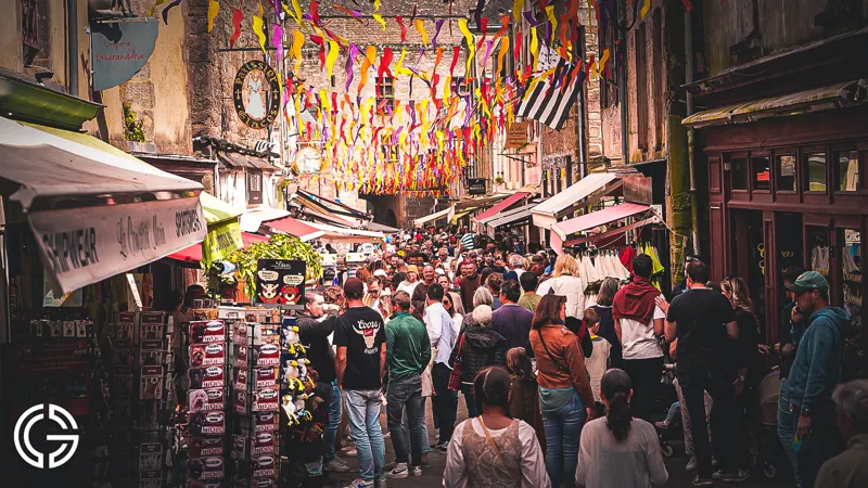 Une rue pavée noire de monde sous des guirlandes colorées pendant une fête médiévale.
